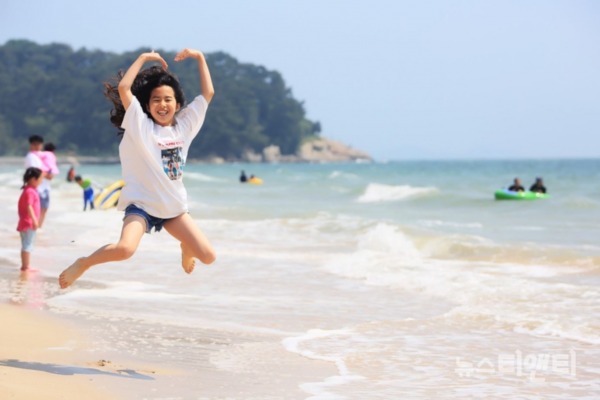 파도가 밀려드는 해변에서 한 여성이 하늘로 높이 뛰어 오르며 기념촬영을 하고 있는 모습. 두 팔은 머리 위로 큰 하트를 그리고 있다. / 대천시 제공