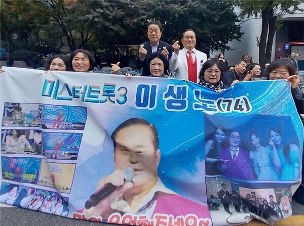 사진 =  미스터트롯3에서 인기를 얻은 인기가수 이생노(74세)와 김용호 서울시의원이 팬클럽과 함께 기념 촬영하고 있다.
