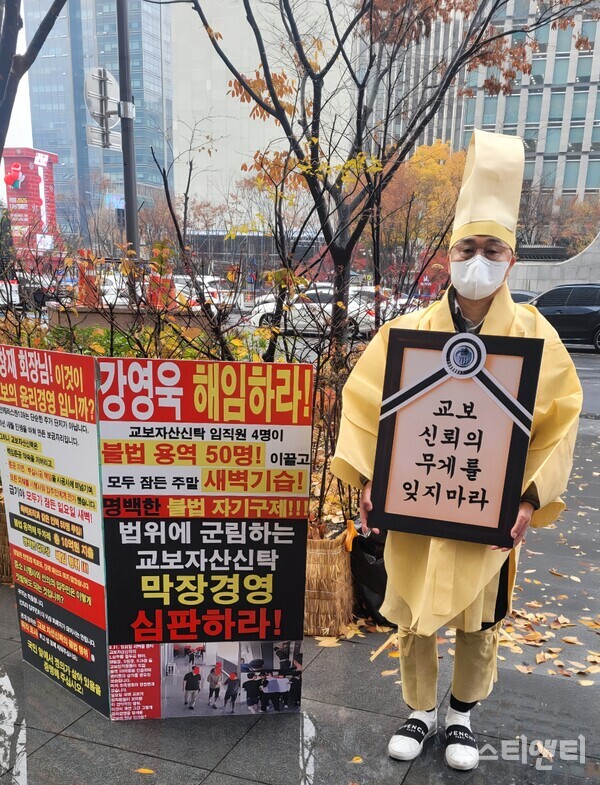 25일 서울 강남구 교보자산신탁 본사 앞에서 시위자가 "교보 신뢰의 무게를 잊지 마라"고 적힌 영정틀을 들고 서 있다. 옆에 놓인 피켓에는 용역 동원 사태에 대한 교보 측의 책임을 묻는 강력한 문구들이 적혀 있다. / 뉴스티앤티
